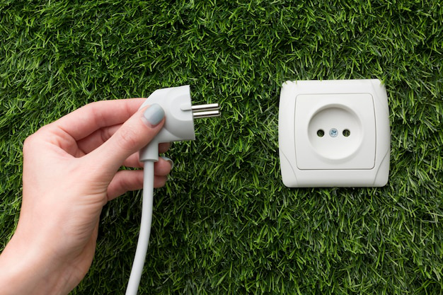 A person holding a plug next to an electric outlet